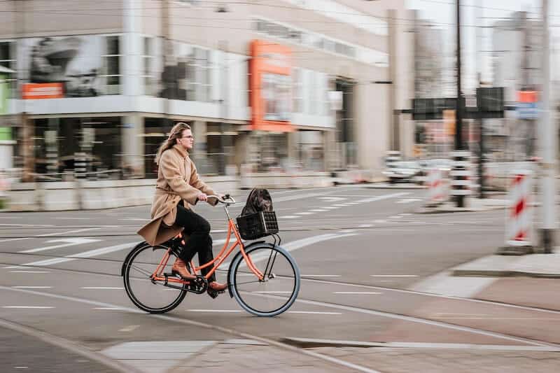 Woman wearing brown coat commuting On a red Bike