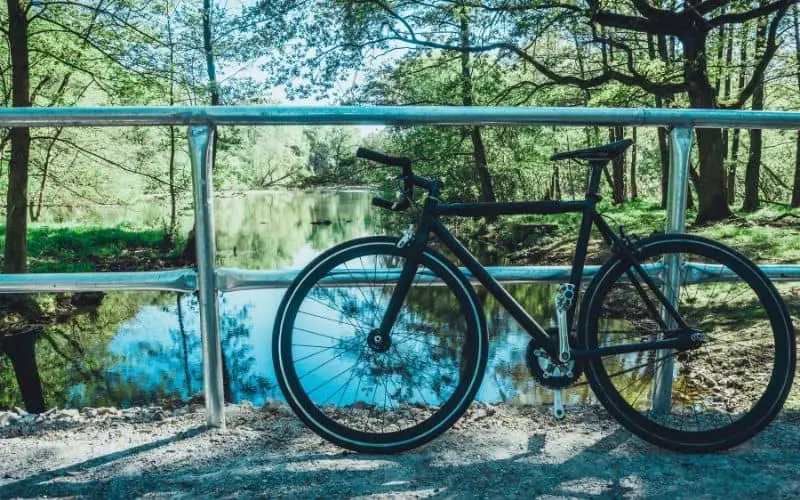 Black single speed bike resting along fence