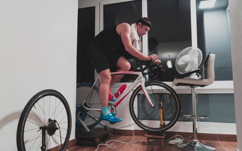 Man indoor cycling with fan and laptop