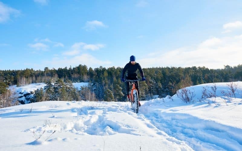 Man mountain biking through the snow with beanie and gloves
